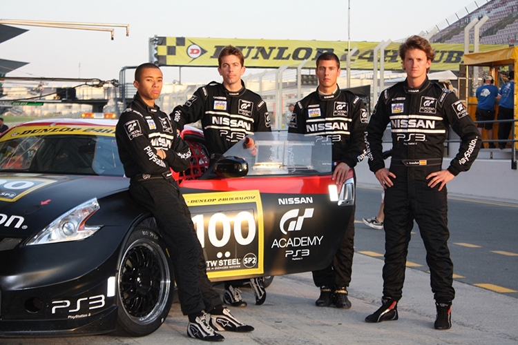 GT Academy drivers wearing black NISMO racing suits standing next to the black #100 race car.
